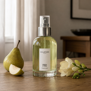 Millefiori Milano Home Spray 100 ml Fresia e Pera op een houten tafel met peer en freesia in zacht raamlicht.