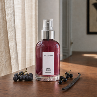Millefiori Milano Home Spray 100 ml Grape Cassis op een houten tafel met druiven, zwarte bessen en vanille in zacht raamlicht.