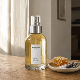 Millefiori Milano Home Spray 100 ml Honey & Sea Salt op een houten tafel met honingraat, zeezout en lavendel in zacht raamlicht.