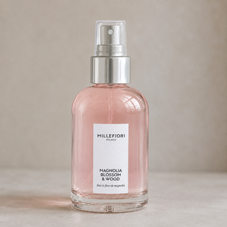 Detailbeeld van Millefiori Milano Home Spray 100 ml Magnolia Blossom & Wood met lichtroze glas, wit etiket en transparante dop over de zilveren verstuiver.
