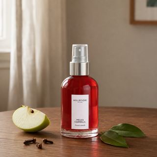 Millefiori Milano Home Spray 100 ml Mela & Cannella op een notenhouten tafel met groene appel, kruidnagel en groene bladeren.