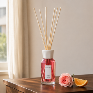 Millefiori Ambra & Rosa geurstokjes op een houten console met roos en sinaasappel.