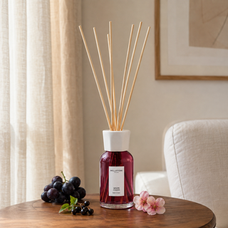 Millefiori Milano Reed Diffuser 250 ml Grape Cassis op een houten bijzettafel met druiven, cassis en bloesem als verwijzing naar de geur.