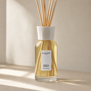 Detail van Millefiori Milano Reed Diffuser 250 ml Honey & Sea Salt met lichtgeel glas, wit etiket, witte kraag en natuurlijke geurstokjes.