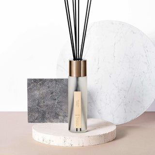 Millefiori Cedar geurdiffuser met zwart riet en goudkleurige dop op marmeren voet