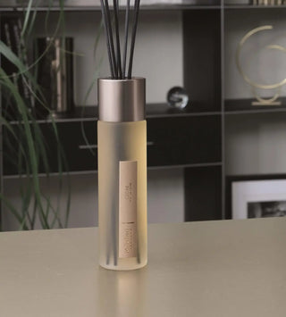 Millefiori Cedar geurdiffuser met zilverkleurige dop en donkere rietjes op tafel