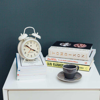 Witte retro wekker met klassiek ontwerp op stapel boeken naast koffiekopje en boekenstapel