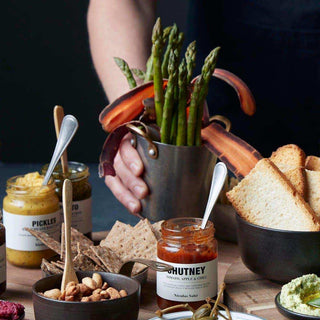Minibucket met groene asperges en wortels, vastgehouden tussen potjes en andere hapjes