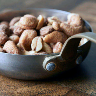 Mini koekenpan gevuld met gemengde noten, met geklonken handvat op een houten tafel
