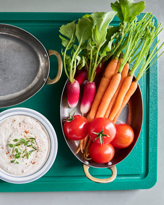 Ovale mini pan met wortels, radijzen en tomaten op een groen dienblad
