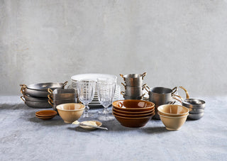 Meerdere kleine pannen met goudkleurige handgrepen tussen servies en glazen