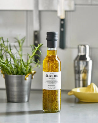 Fles olijfolie met rozemarijn op een aanrecht naast een kruidenplant en citruspers