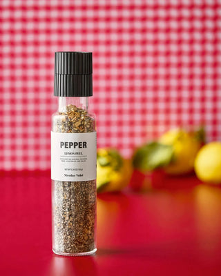 Nicolas Vahe pepermolen met lemon pepper op een rood oppervlak, met citroenen op de achtergrond