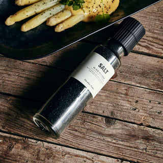 Nicolas Vahé zoutmolen met zwart zeezout op houten tafel naast een bord met asperges