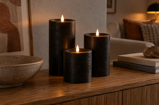 Drie zwarte LED-kaarsen op een houten dressoir in een warme woonkamer